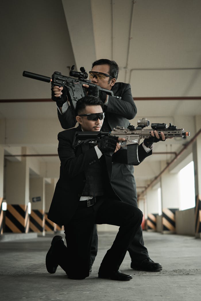 Two men in suits with rifles in an action scene inside a parking garage.