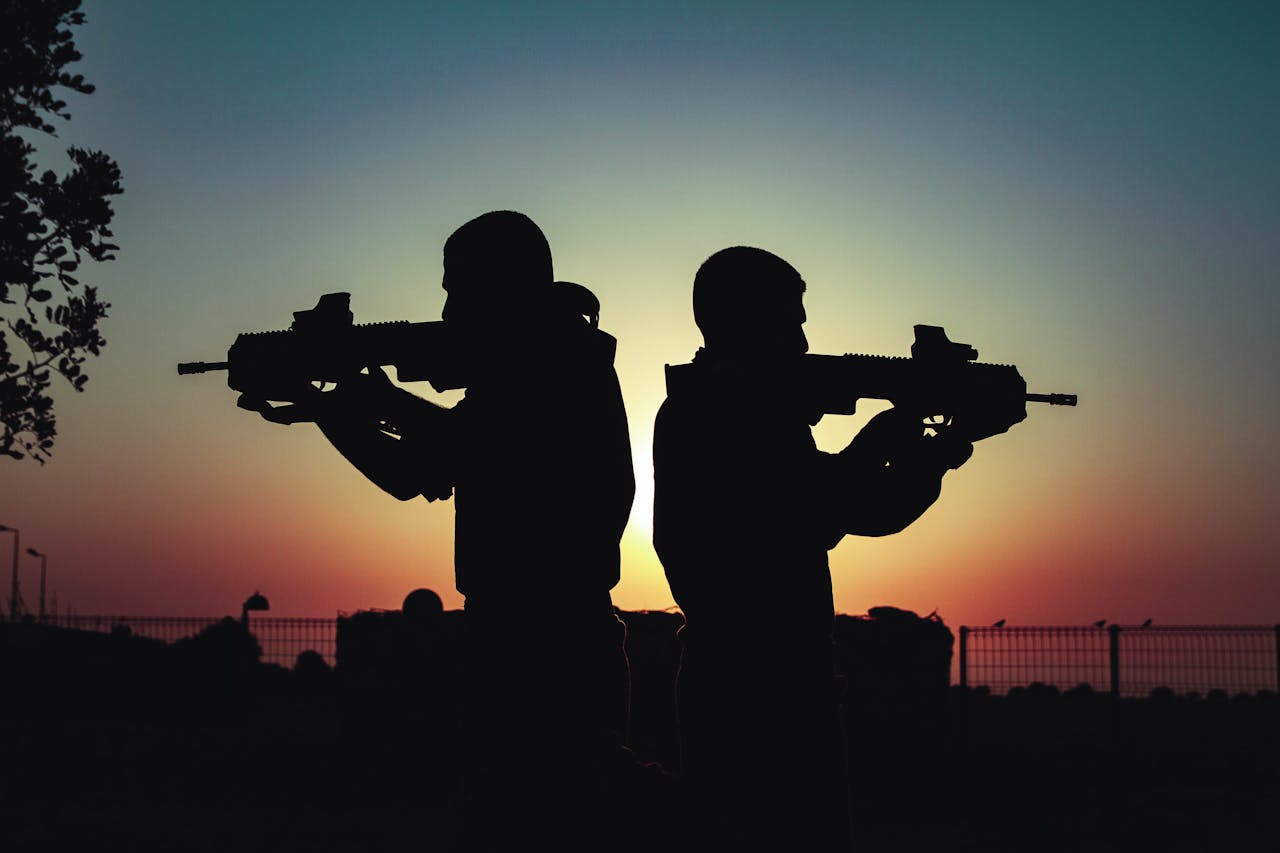 Silhouette of two soldiers with rifles against a vivid sunset sky, creating a dramatic scene.
